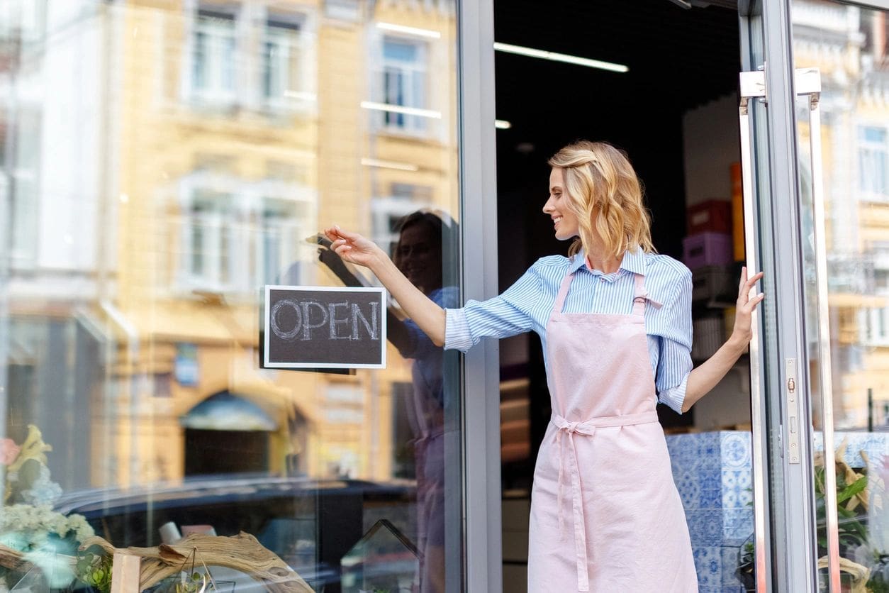 A woman in an apron is standing outside of a store.